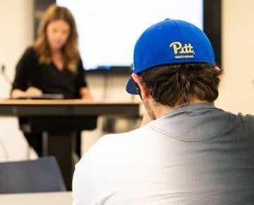 Student seated in class wearing Pitt-Greensburg hat