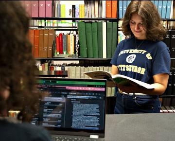 A student looks inside a book while at the campus library.