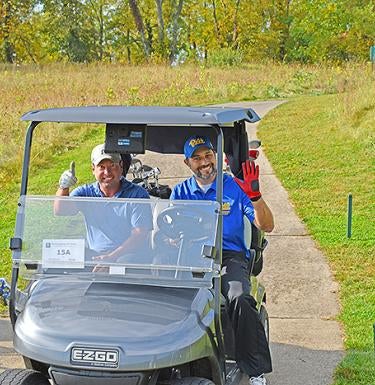 Two alumni golfers in golf cart